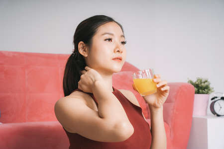 Beautiful pregnant asian woman drinking orange juice after exercise at home.