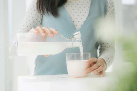 Close up shot - Young beautiful pregnant asian woman pouring fresh milk from a bottle.の写真素材