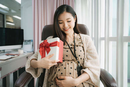 Beautiful pregnant asian businesswoman open a present gift box from husband.の写真素材