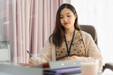 Beautiful pregnant adult asian thai businesswoman working in office.の写真素材