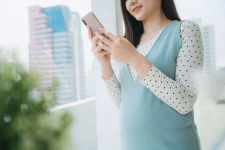 Young beautiful pregnant asian thai woman using smartphone at home.の写真素材