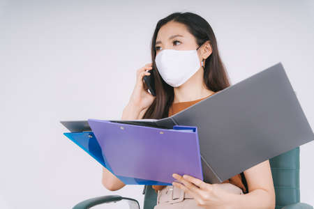 Beautiful asian thai businesswoman wearing mask talking on the phone reading report isolate over...