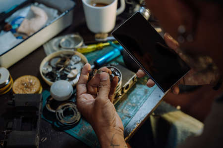 A man fix the film camera and clean the dust on the lens then assemble all the part together, look at the cleaning tutorial on internet by smartphone.の写真素材