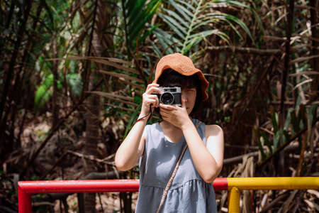 Young asian Thai woman traveler with vintage camera at country side road. Local trip.