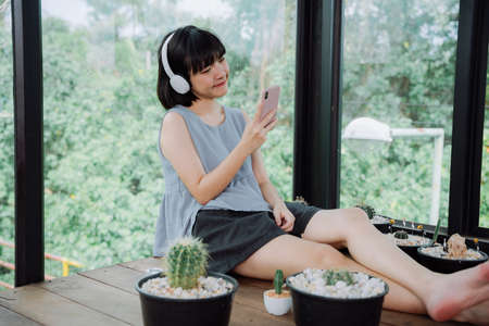 Beautiful asian thai woman enjoy listen to music with wireless headphone and smartphone at local cactus farm hostel.の写真素材
