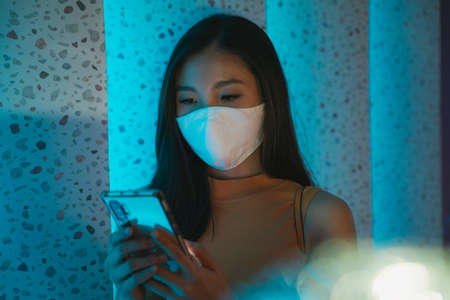 Close up portrait - Beautiful asian thai woman wear cotton mask using smartphone in nightclub.の写真素材