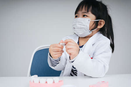 Pretty asian thai kid play role as doctor and dentist wear mask fixing teeth toy.の写真素材