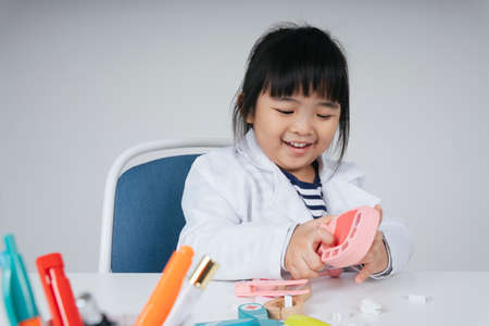 Pretty asian thai kid play role as a dentist fixing teeth toy.