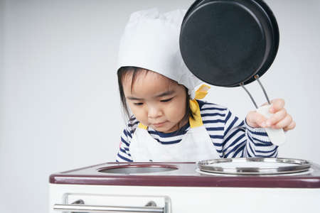 Pretty asian thai kid play role as a chef cooking food at cooker station with oven.の写真素材