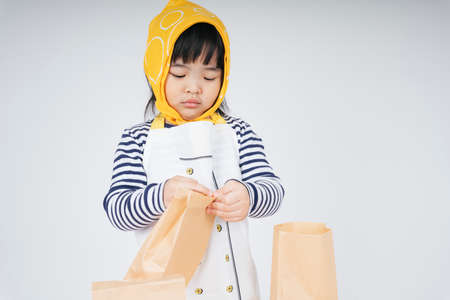 Pretty asian thai kid play role as a waitress wearing yellow bandage packing food in paper bag.