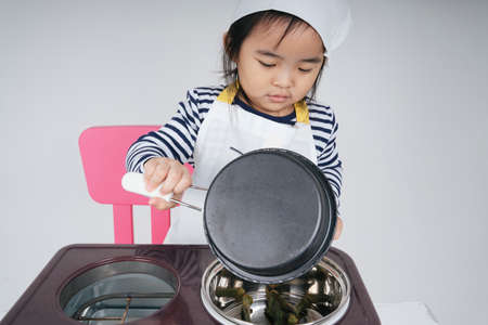 Pretty asian thai kid play role as a chef cooking food at stove station.