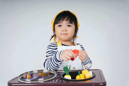 Pretty asian thai kid play role as a chef wearing yellow bandage cooking food with stove in kitchen.