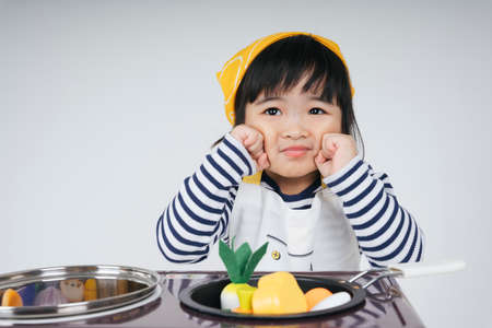 Pretty asian thai kid play role as a chef wearing yellow bandage with stove cooker in kitchen.の写真素材