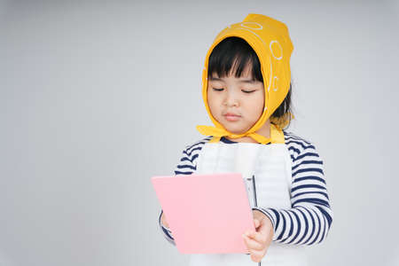 Pretty thai kid play role as a waitress wearing yellow bandage taking order from customer with paper and pen.の写真素材