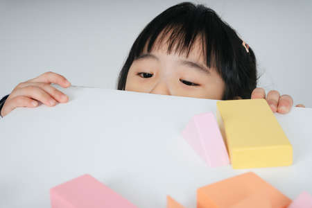 Pretty asian thai kid woman sitting under table looking at toy block.の写真素材