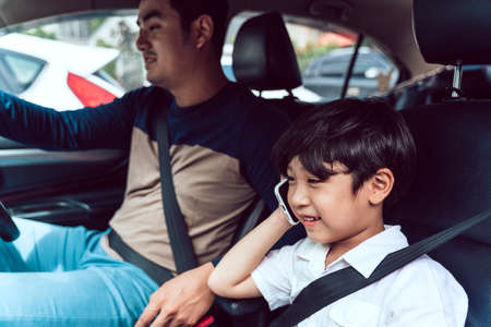 Asian son talking on the phone in the car while father driving.の写真素材