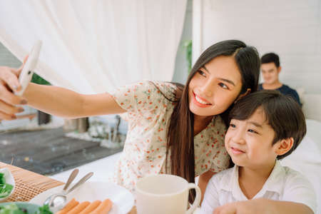 Asian thai mother and son taking selfie with smartphone while having lunch.