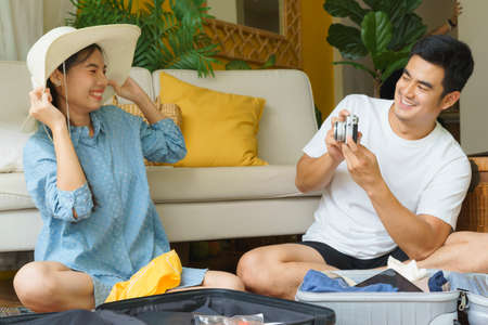 Asian thai couple having fun while packing stuff in hotel room. Man taking photo of his wife with...