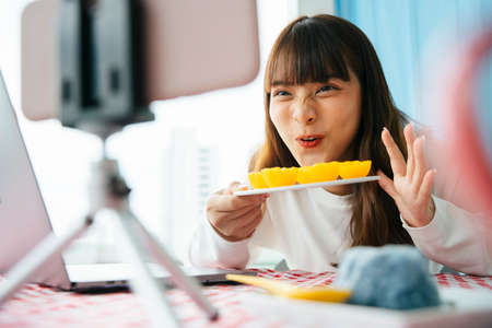 Young asian dark hair woman doing thai dessert food review with golden cake infront of smartphone...