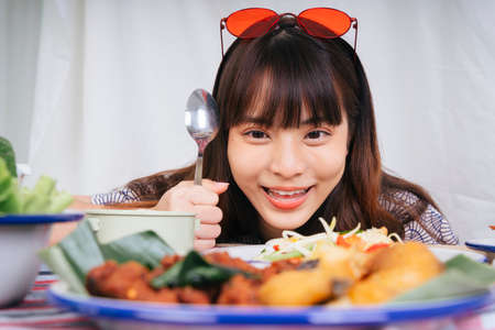 Portrait of drooling young asian woman holding spoon looking at Isan food on table.
