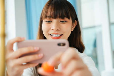Close up portrait of young asian dark hair woman taking photo of pastel fruit shaped mung bean.の写真素材