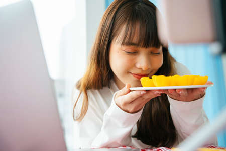 Young asian dark hair woman doing thai dessert food review with golden cake infront of smartphone...