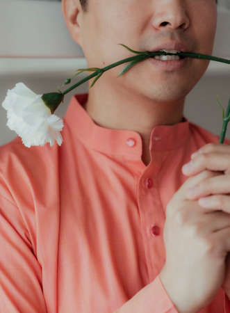 Cropped image of white carnation is bite by the man in orane mandarin collar.