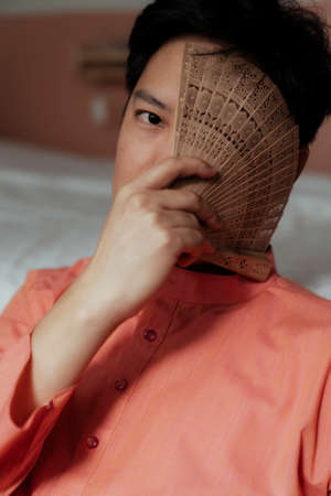 A black hair gay look at the camera with one eye while he cover another his eye with folding fan.の写真素材