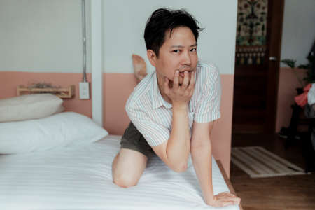 Portrait shot of asian gay in stripped shirt on the bed with a weird posture like a cat.