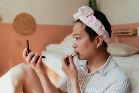 Asian gay in pink headband apply the red lipstick in front of the small mirror.