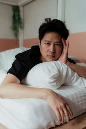Asian gay in black t-shirt wakke up with headache 'cause he's sleepless due to it's noisy outside.