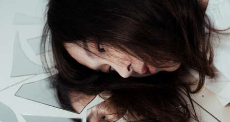 Curly long hair girl lie down on the broken mirror that represent her broken mind.