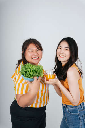Two asian healthy women with salad bowl and orange juice on white background.の写真素材