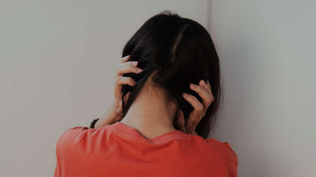 Woman in orange t-shirt sit at the room's corner, cover his ears try to ignore the voice in her...