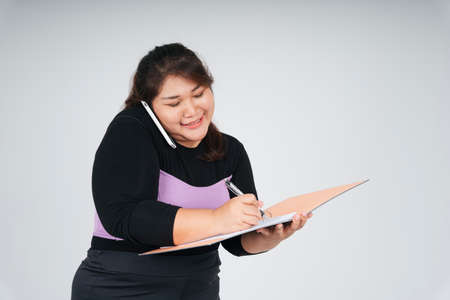 Busy asian chubby business woman talking on the phone and working on document papers.の写真素材
