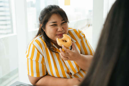 Asian chubby woman enjoy unhealthy eating sweet dessert donut with friends in office.