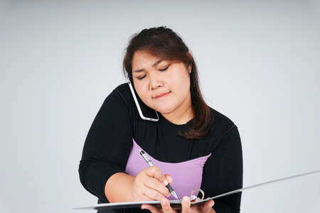 Busy asian chubby business woman talking on the phone and working on document papers.