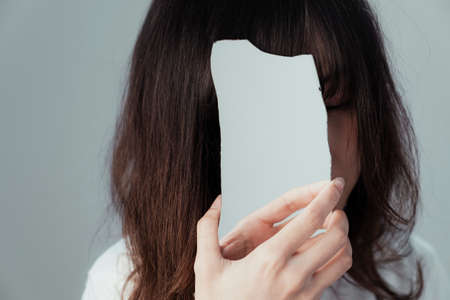 Curly long hair girl raise a piece of mirror to cover all of her face.の写真素材