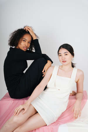 Fashion portrait of asian woman in white dress and african woman in black dress.の写真素材