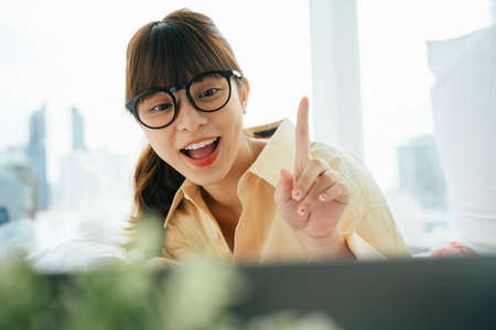 Cheerful happy young asian dark hair woman wearing eyeglasses doing video call on computer latpop.