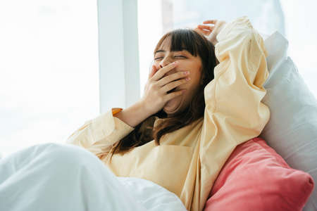 Sleepy young asian dark hair woman wake up in the morning on a bed.の写真素材