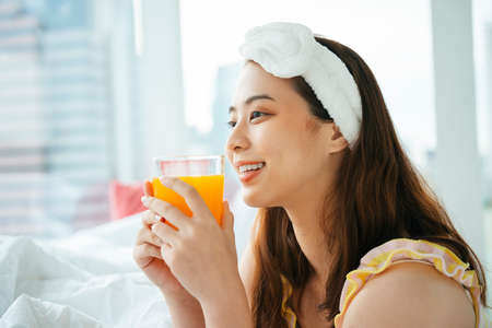 Young asian dark hair woman wearing white headband holding glass of orange juice.の写真素材