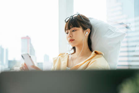 Young asian dark hair woman listen to music with earphones and smartphone in bedroom.の写真素材