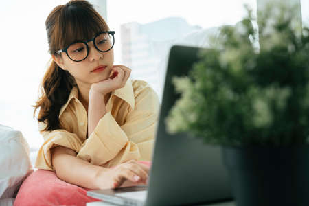 Young asian dark hair woman wearing eyeglasses working on laptop at home.の写真素材