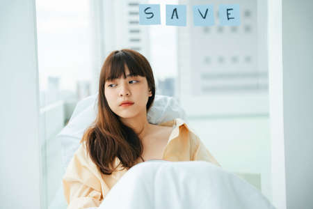 Young asian dark hair woman laying on a bed in bedroom due to coronavirus pandemic.の写真素材