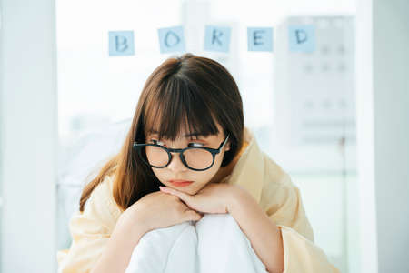 Cute young asian dark hair woman wearing eyeglasses laying on a bed. Bored girl relax on a couch.の写真素材