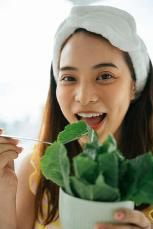 Young asian dark hair woman with white headband enjoy eating organic vegetable salad.