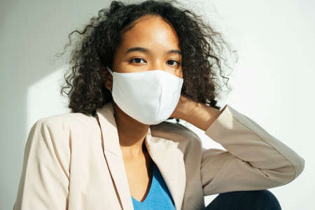 Fashion portrait of african curly hairstyle woman wear white mask, business jacket, and jeans pants.の写真素材