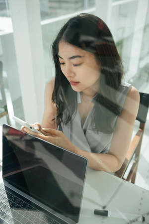 Busy beautiful asian business woman using smartphone working in office.の写真素材