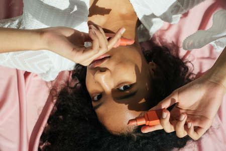 Top view - African curly hair woman holding red lipstick on pink cloth background.の写真素材